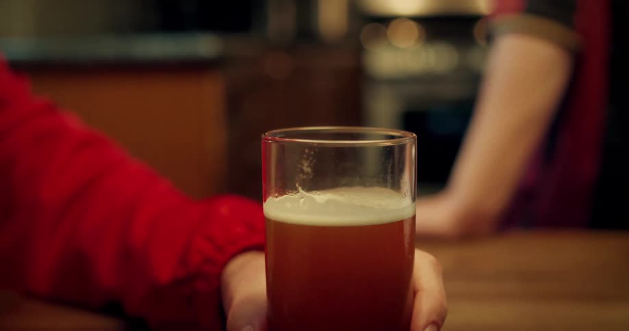 A close-up shot of a hand sliding a pint of beer across a wooden table, slowly coming into focus