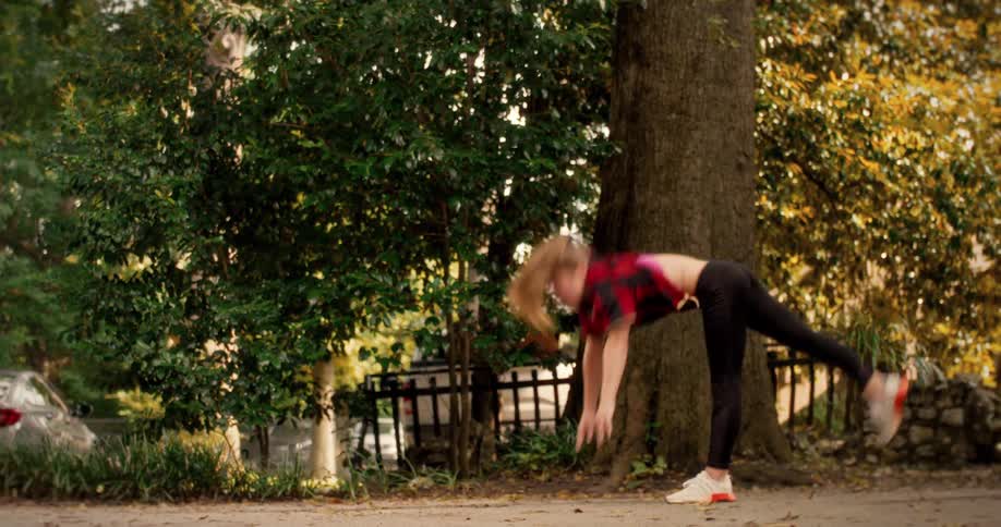 A quirky father and his talented daughters practice gymnastics, doing cartwheels and handstands in slow motion on a sidewalk