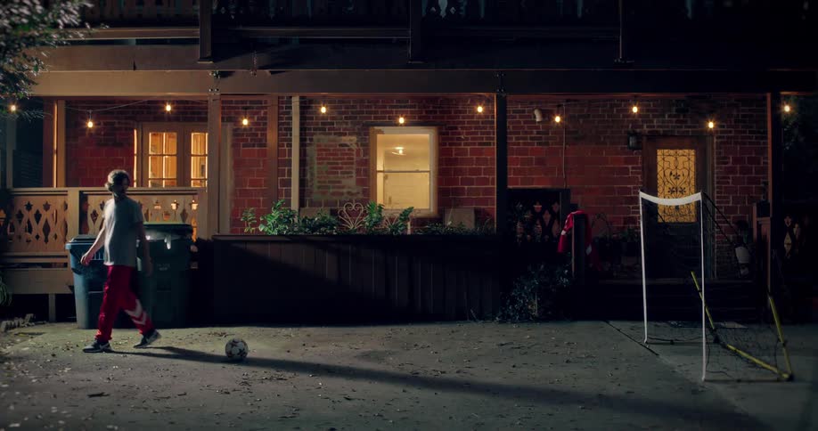 A young soccer player practices alone at night in their backyard, scoring a goal and celebrating their dedication