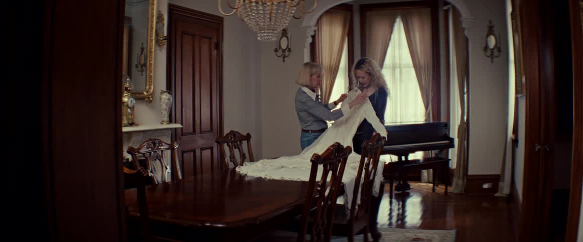 A mother and daughter share a loving, emotional moment as they look at a beautiful wedding dress together in their home