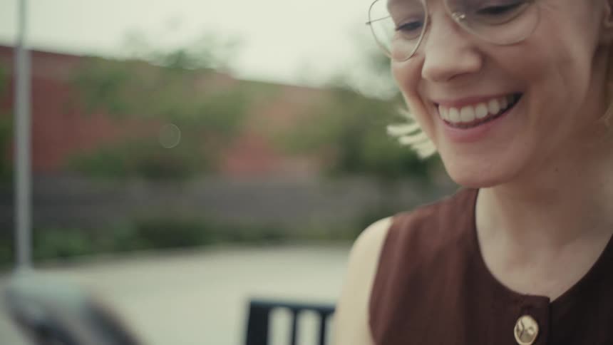A happy blonde woman with glasses smiles while scrolling on her smartphone outdoors