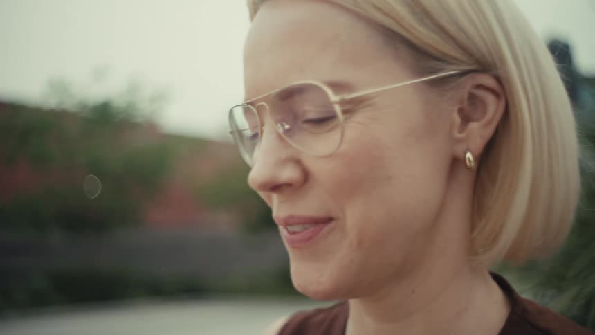Close-up of a smiling blonde woman in glasses scrolling on her smartphone outdoors