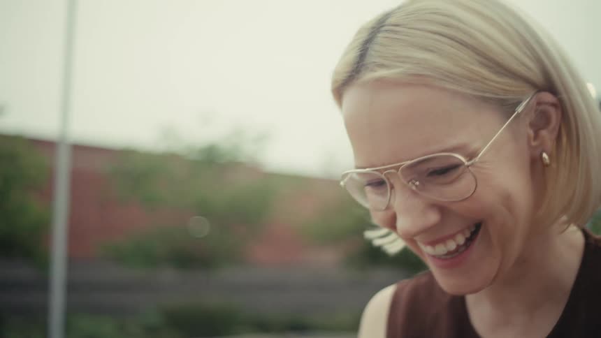 Close-up in slow motion of a joyful blonde woman laughing while watching something on her smartphone outdoors
