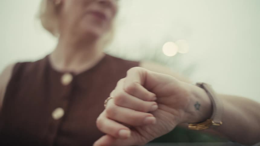 A woman checks her phone and then smiles while looking at her watch outdoors
