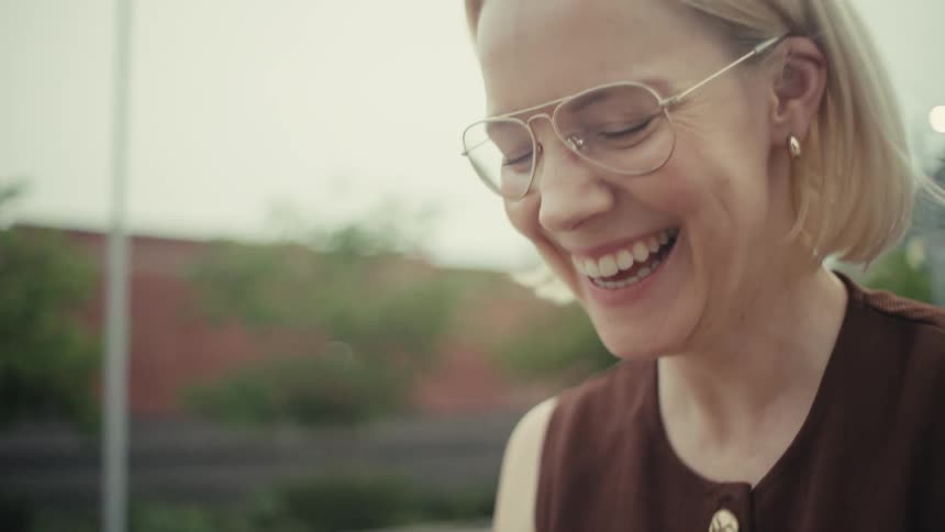 A slow focus pull reveals a happy blonde woman with glasses laughing while looking at her smartphone