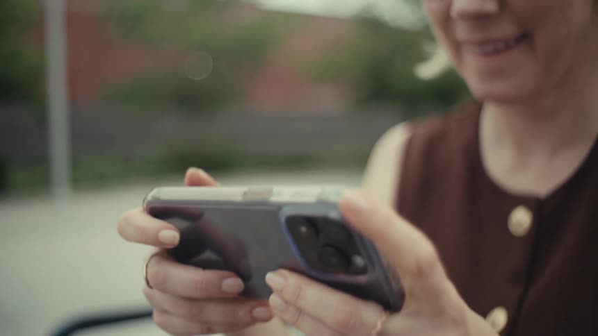 Slow motion close-up of a smiling blonde woman with glasses watching a funny video on her smartphone outdoors