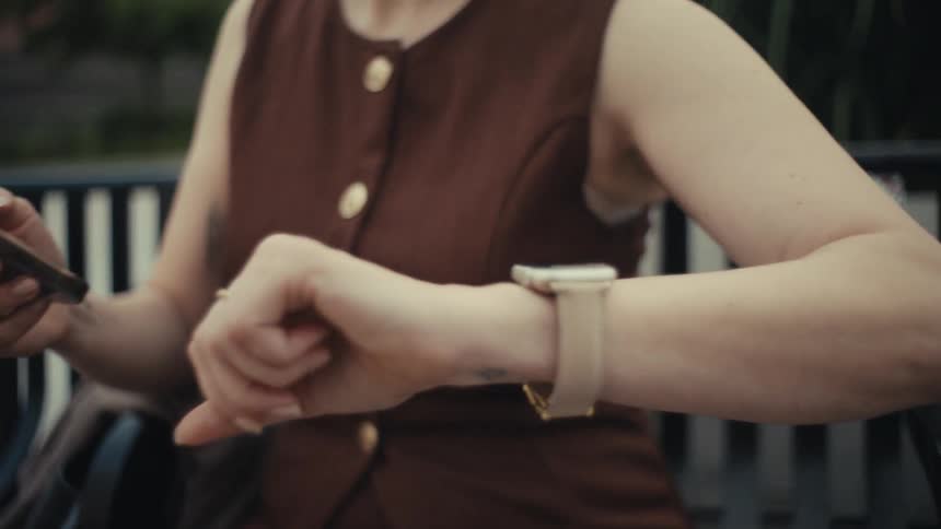 A woman checks the time and notifications on her modern smartwatch while relaxing outdoors on a bench