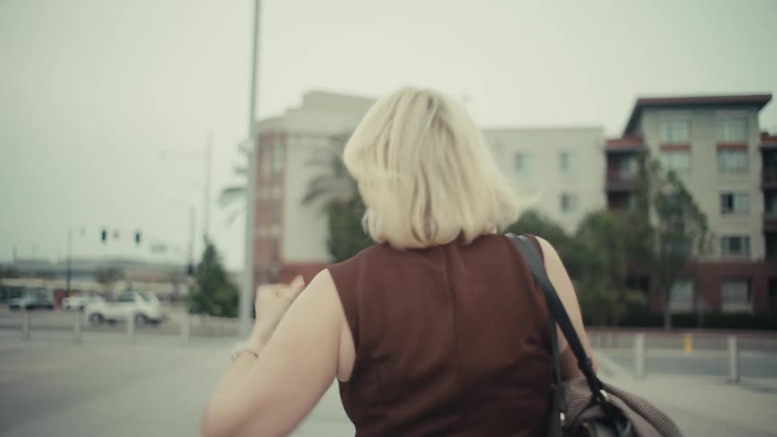 A businesswoman with blonde hair walking through the city receives good news on a phone call and celebrates with a fist pump in slow motion