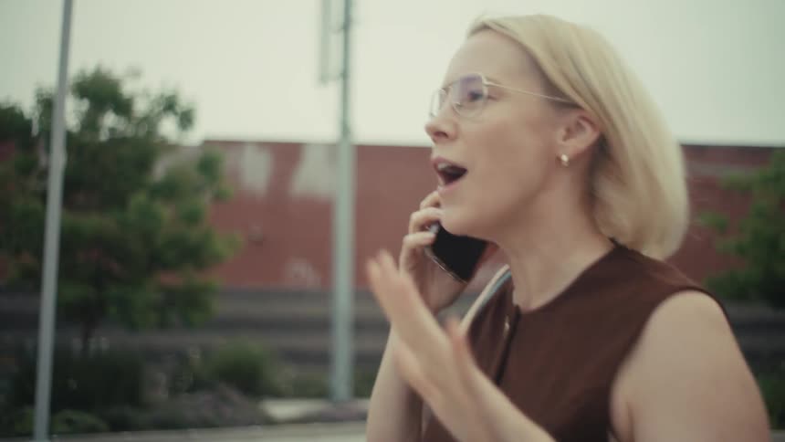 An ecstatic professional woman walking in the city receives great news on her phone and celebrates enthusiastically in slow motion