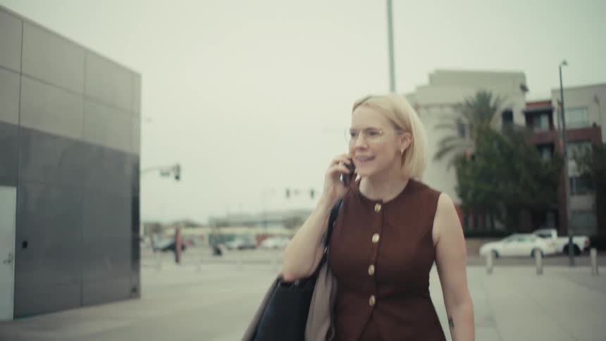 A professionally dressed businesswoman experiences a rollercoaster of emotions from joy to shock to celebration while on a phone call in the city