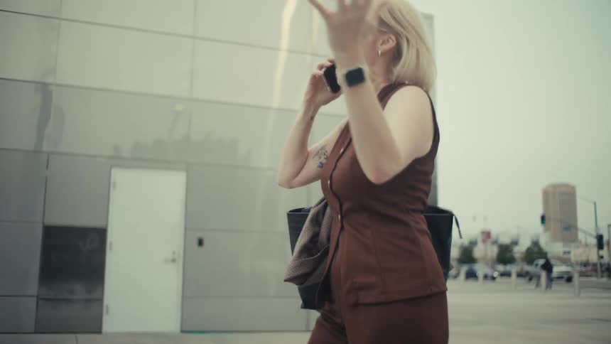 Slow motion shot of a joyful businesswoman walking down the street, pumping her fist and shouting with excitement during a phone call