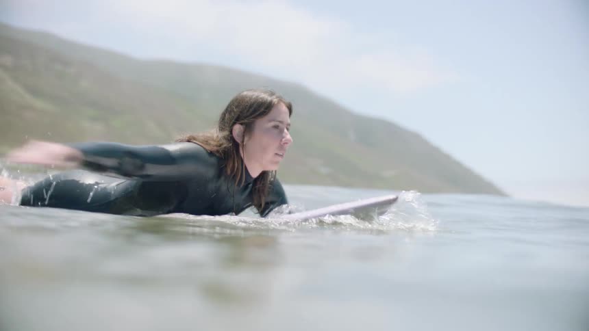 Shot from the water's surface of a female surfer paddling on her board out into the ocean