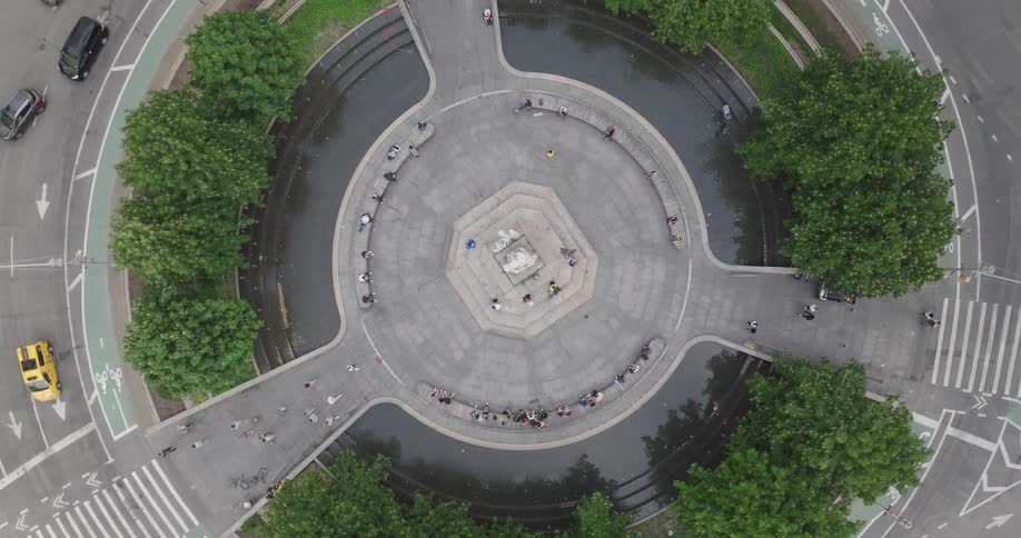 A rising top-down aerial shot captures the serene center of Columbus Circle in New York City, slowly revealing the bustling traffic of cars and taxis circling the landmark