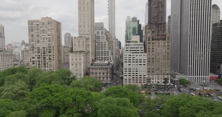 An aerial view pushes in from Central Park towards the towering skyscrapers of the Manhattan skyline on a cloudy day