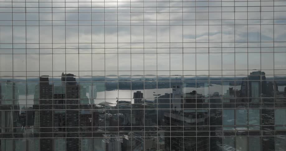 A slow-moving aerial shot captures the abstract reflection of a sprawling cityscape and river in the glass facade of a modern skyscraper