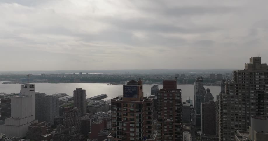 An aerial shot pushes forward between skyscrapers to reveal the expansive New York City skyline and the Hudson River on an overcast day
