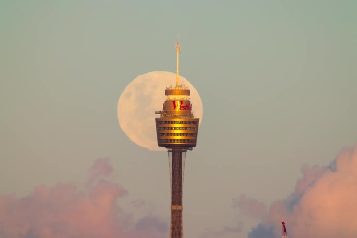 A breathtaking time-lapse shows the full moon rising behind the Sydney Tower Eye amidst beautiful pink sunset clouds