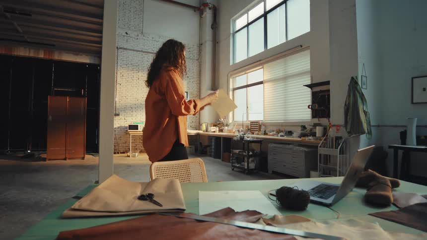 A creative female artisan inspects a paper design pattern in her spacious, sunlit industrial loft studio