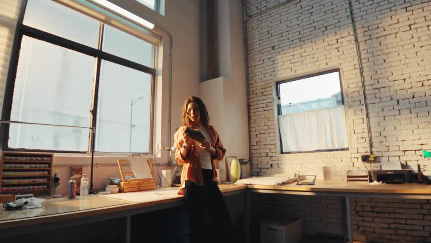 A young female shoe designer proudly inspects a finished shoe in her sun-drenched industrial loft workshop