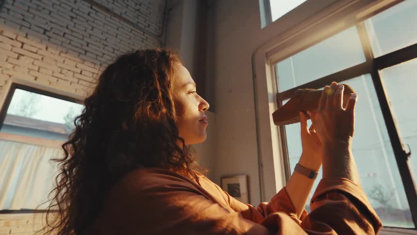 A female shoemaker proudly inspects a handcrafted shoe, admiring her work in the warm, golden light of her workshop