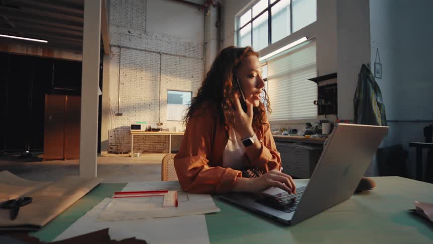 A busy female entrepreneur talks on the phone while sketching a new design in her industrial workshop
