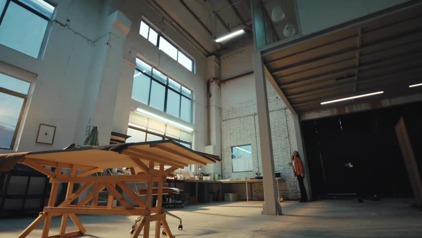 A young female artist or designer walks into her new, spacious industrial loft studio, turns on the lights, and looks around thoughtfully