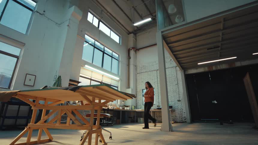 A young female artist or designer walks into her new, spacious industrial loft studio, turns on the lights, and looks around thoughtfully