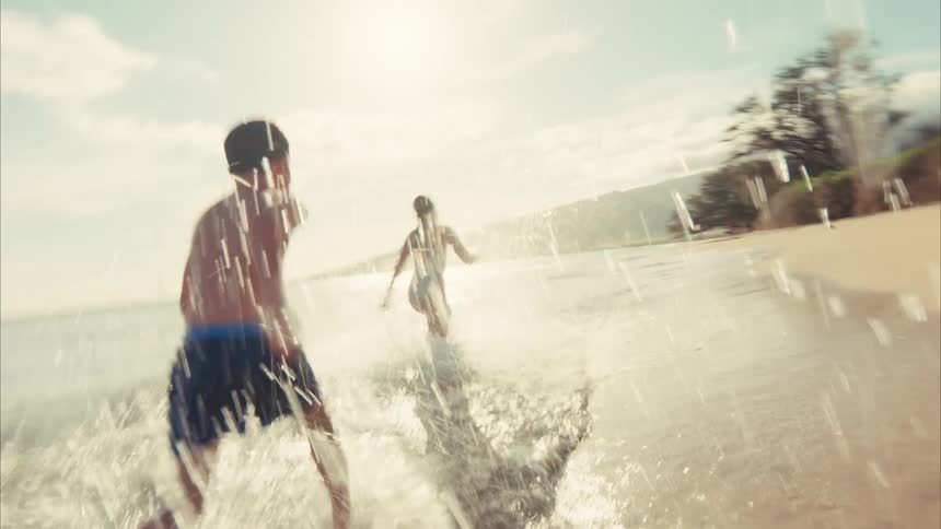 Slow-motion footage from a low angle shows two happy kids running and playing in the shallow waves of a sunny beach