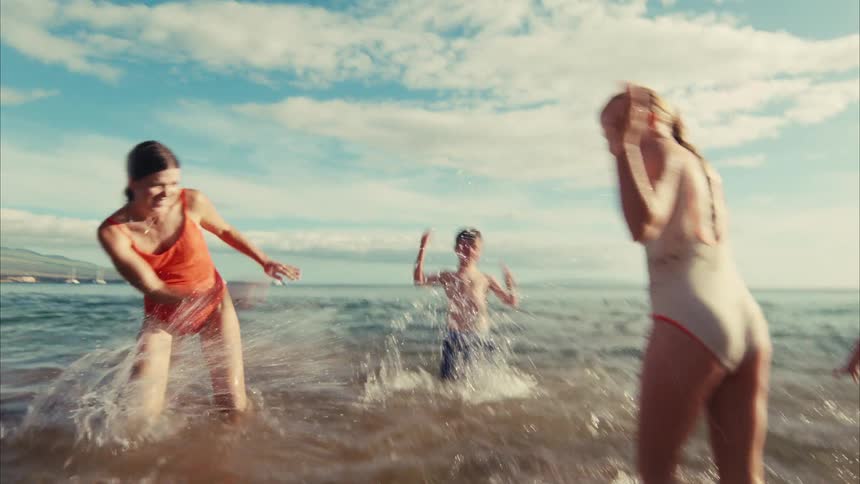 A joyful family playfully splashes each other in the shallow ocean waters in this fun, slow-motion, vintage-style shot