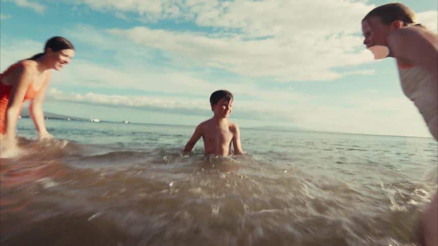 A joyful family playfully splashes each other in the shallow ocean waters in this fun, slow-motion, vintage-style shot