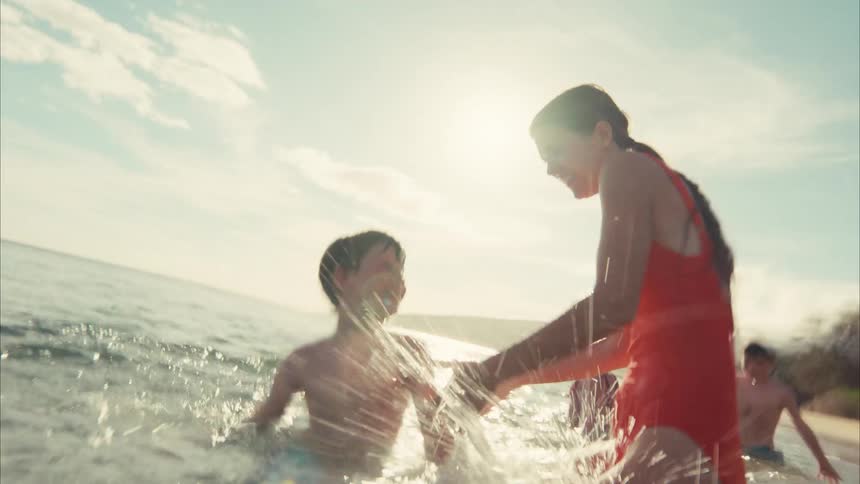 A group of happy children splash water at the camera while playing in the ocean on a sunny day