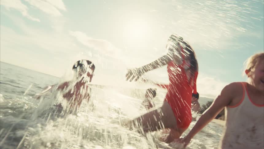 A group of happy children splash water at the camera while playing in the ocean on a sunny day