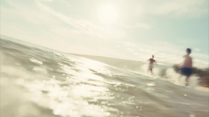 A happy young boy runs and splashes through the shallow ocean water in cinematic slow motion on a bright sunny day at the beach