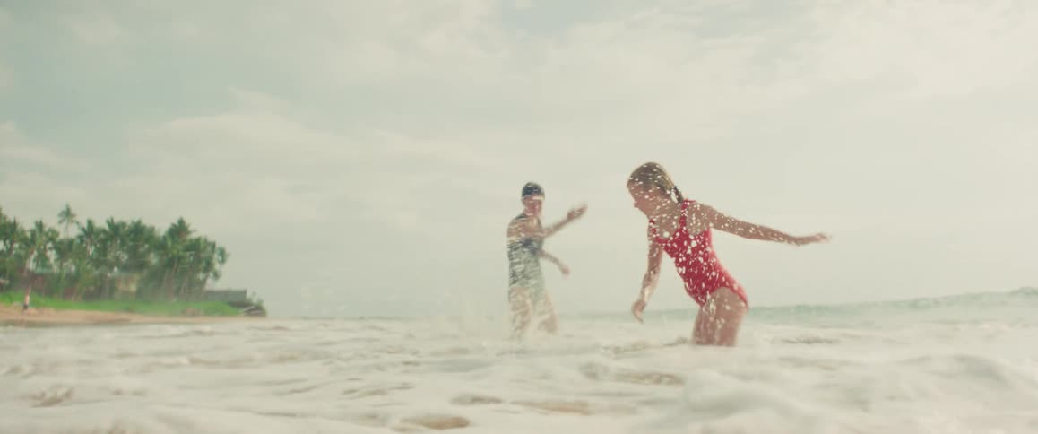 Two women in swimsuits playfully splash each other in the ocean waves on a tropical beach in slow motion