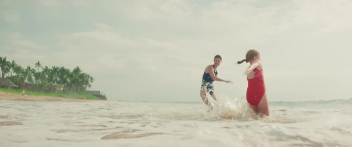 Two women in swimsuits playfully splash each other in the ocean waves on a tropical beach in slow motion
