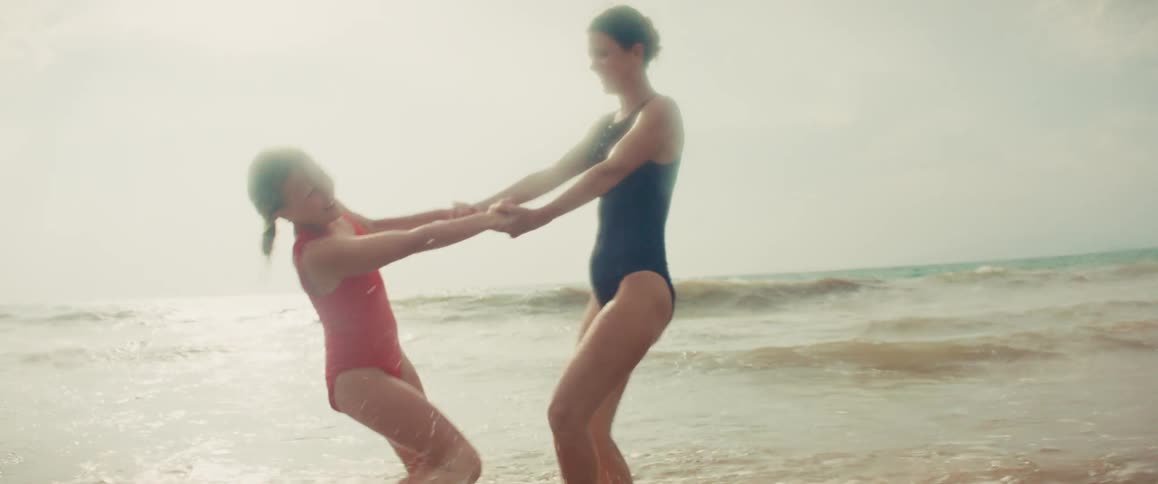 A joyful mother and daughter hold hands and spin around in the shallow ocean water