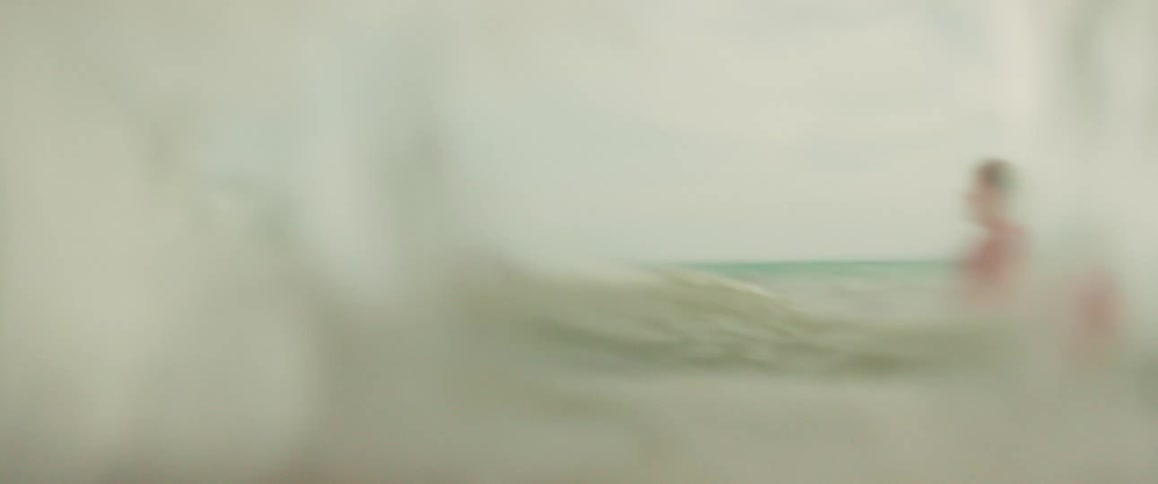 A happy mother holds her son as they brace for a wave to crash over them while playing in the ocean in slow motion