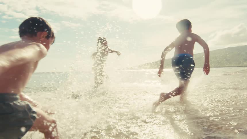 Slow motion shot of three young friends running joyfully through the splashing waves at a sunny beach