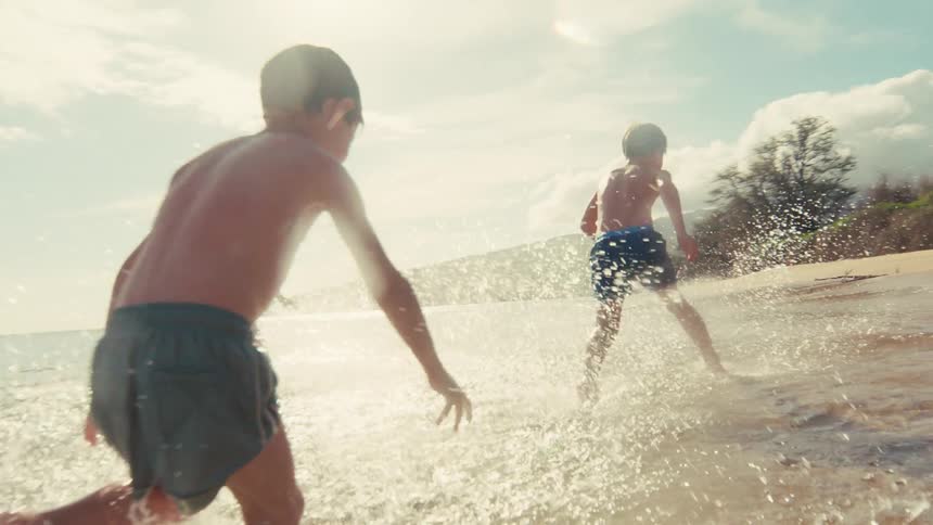 Slow motion shot of three young friends running joyfully through the splashing waves at a sunny beach