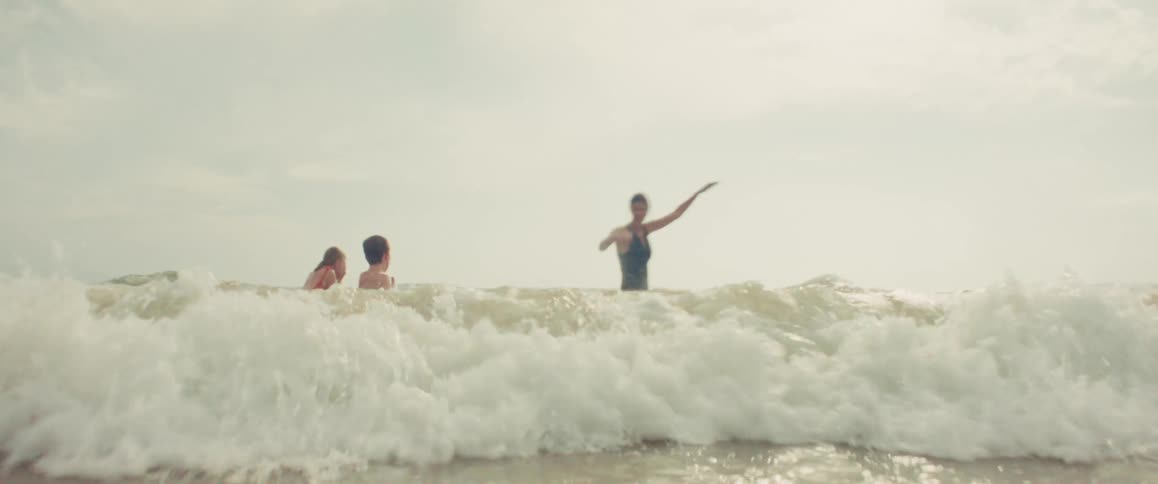 A mother and her two children jump and play in the ocean waves in a beautiful slow-motion shot from the water's perspective