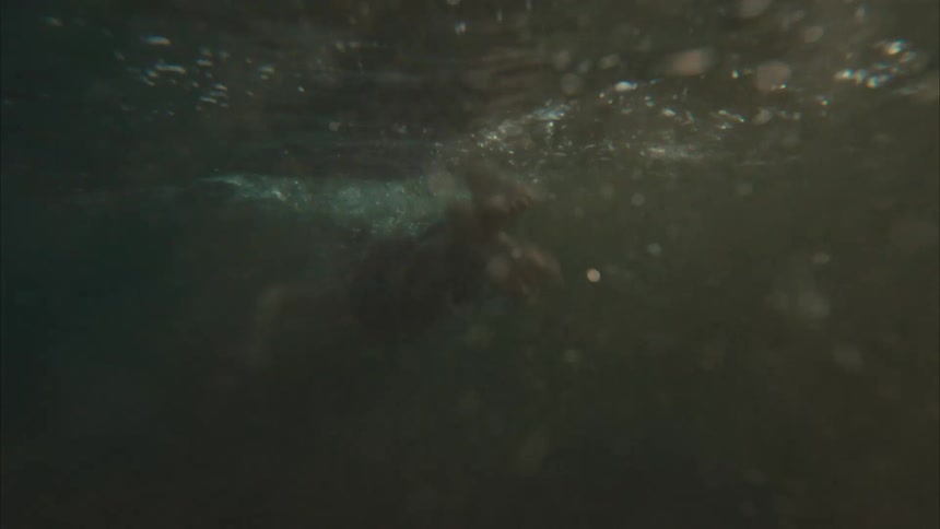 A young boy wades in the ocean before the camera submerges to follow him swimming underwater in slow motion