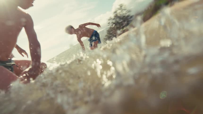 Joyful children run and splash through the ocean waves on a sunny tropical beach in slow motion
