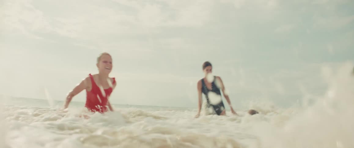 A happy family of a mother, daughter, and son playfully jump and splash as a foamy ocean wave washes over them in slow motion