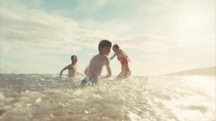 A joyful family with young children playfully splashes each other in the ocean waves in cinematic slow motion