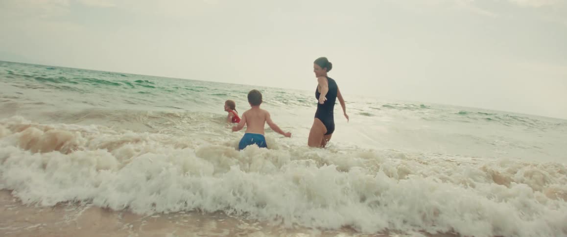 Happy family with two children run and splash together in the ocean waves on a summer beach vacation