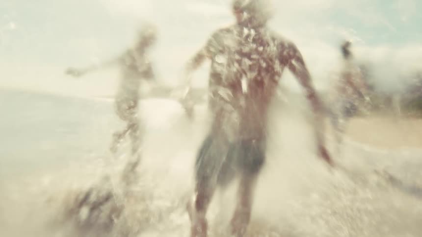 Three carefree children run and splash in the shallow ocean waves on a bright sunny day in slow motion