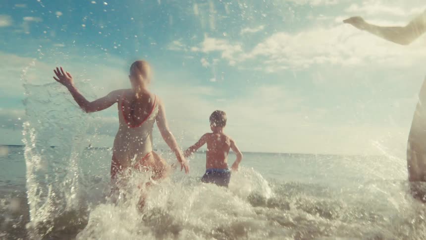 Carefree children joyfully run and splash into the ocean waves in cinematic slow motion