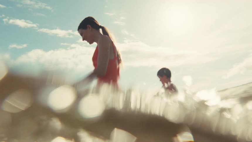 A happy mother in a red swimsuit enjoys a sunny day at the beach, playing in the shimmering ocean water with her children