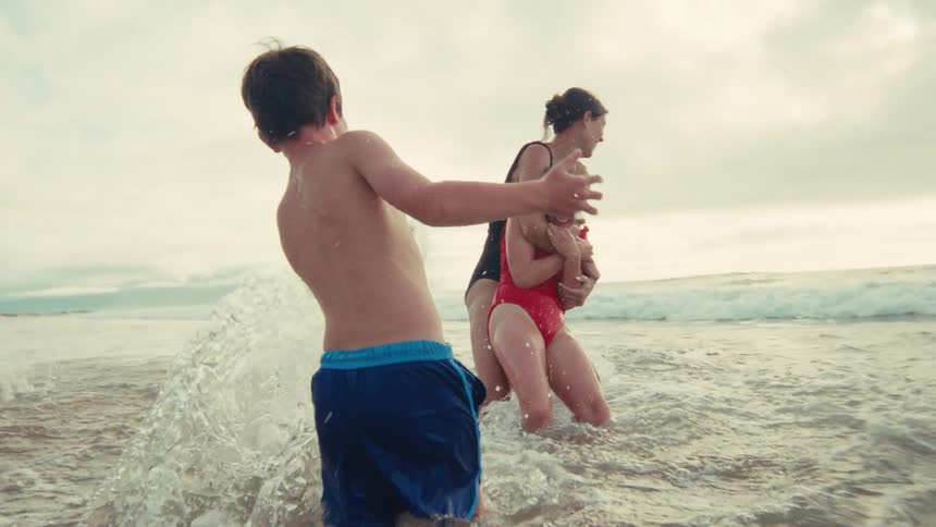A joyful family splashes and plays together in the ocean waves during a beach vacation in slow motion