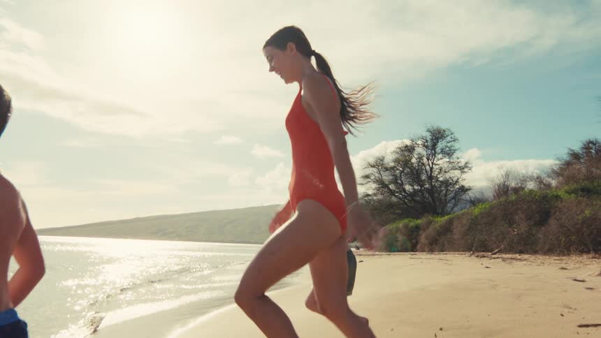 Slow motion shot of a happy mother and her two young sons running together on a beautiful sunny beach